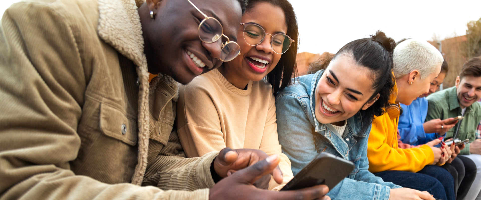 Happy young people looking at a mobile phone together outdoors.