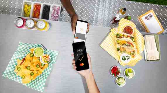 A person holding a smartphone taps it against another smartphone over a food truck counter. 
