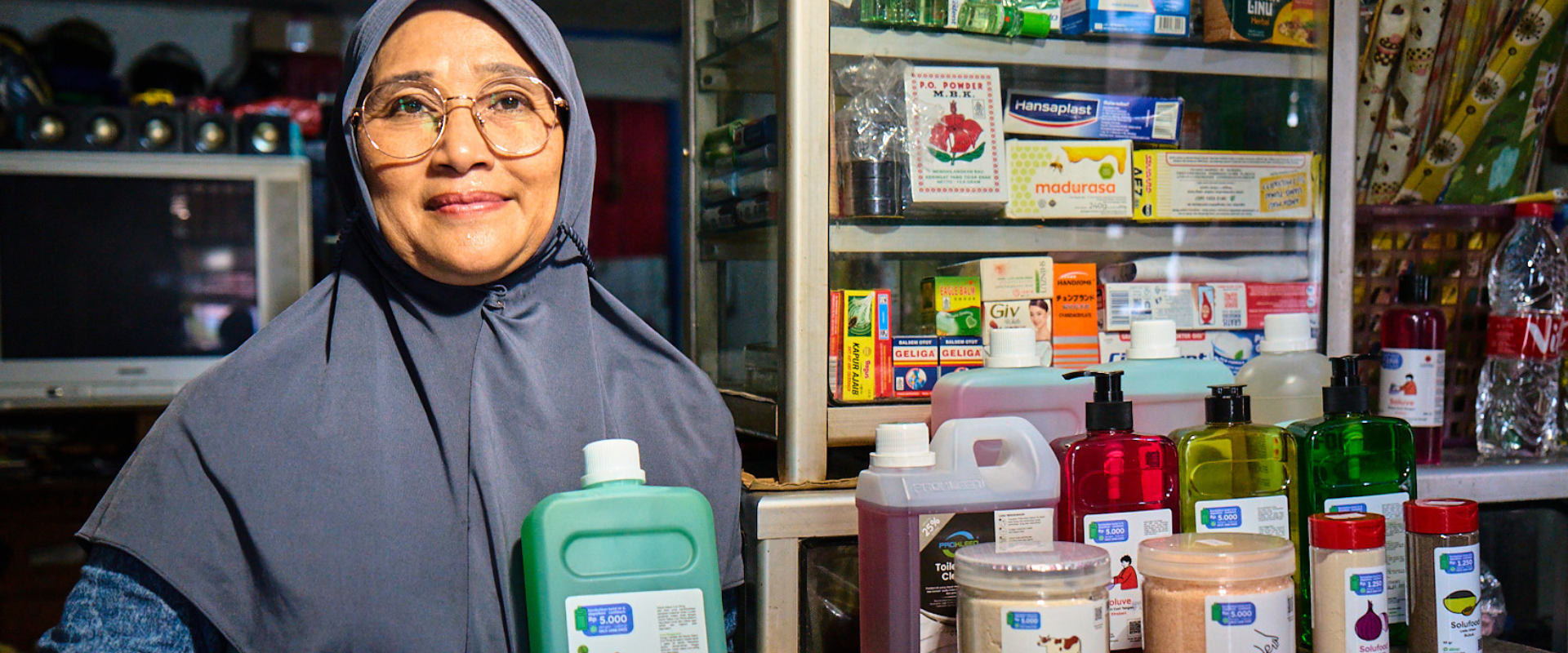A Jakarta shopkeeper holds a reusable bottle in front of a display of other sustainably packaged items in her shop. 