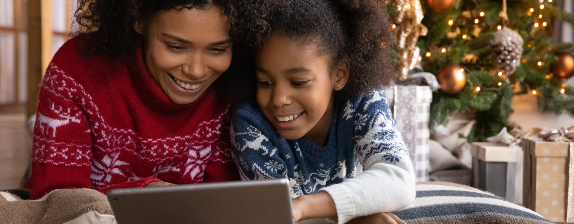 A mother and daugher look at a tablet with a Christmas tree in the background.