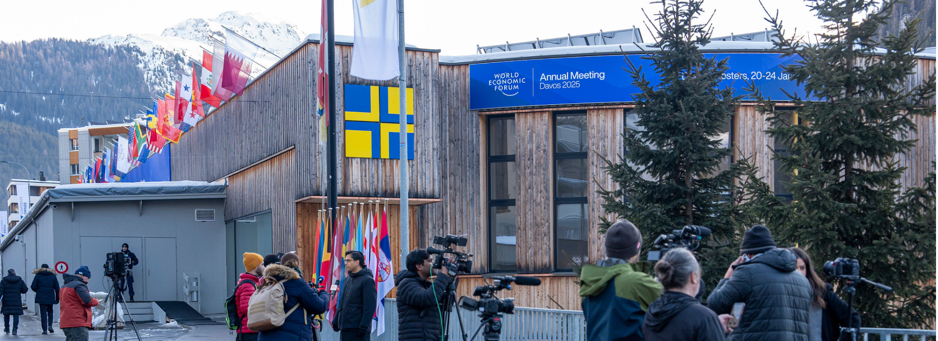 The exterior of a building where Davos 2025 is being held, with flags along the roofline and camerapeople setting up in front.
