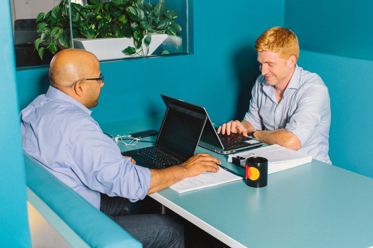 Twee mannen zitten aan een tafel met hun laptops