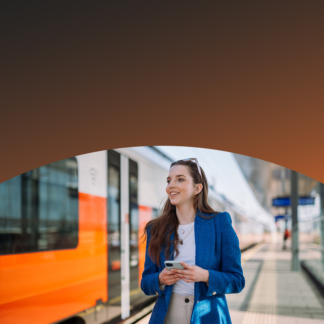 Smilende kvinne venter på metroen med telefonen.