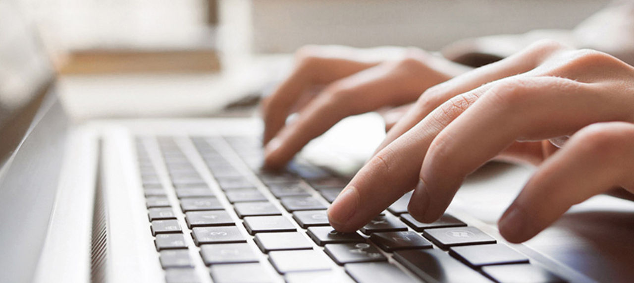 Nærbilde av hender som skriver på tastaturet til en bærbar datamaskin.