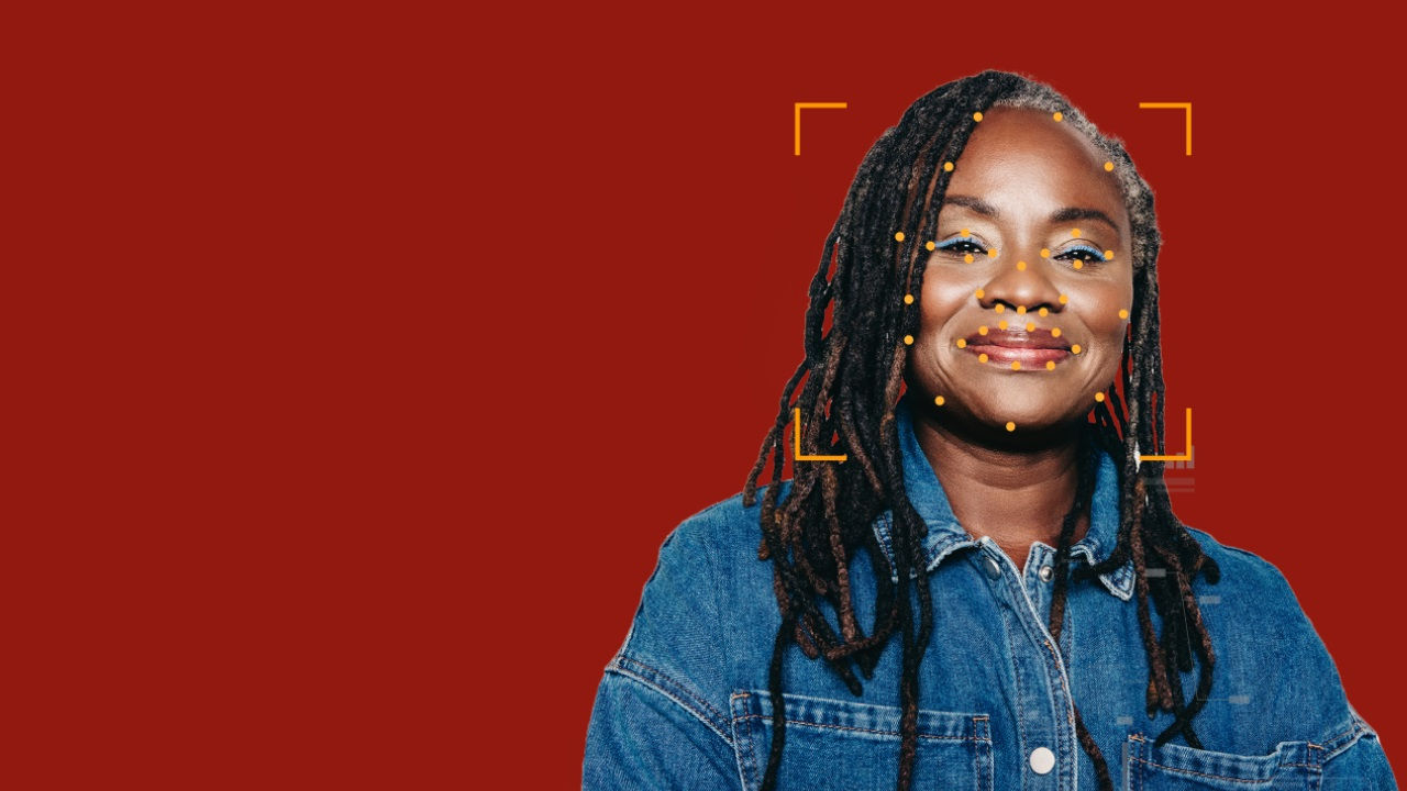 A woman with braids wearing a denim shirt smiles with an overlay showing biometric points on her face. 