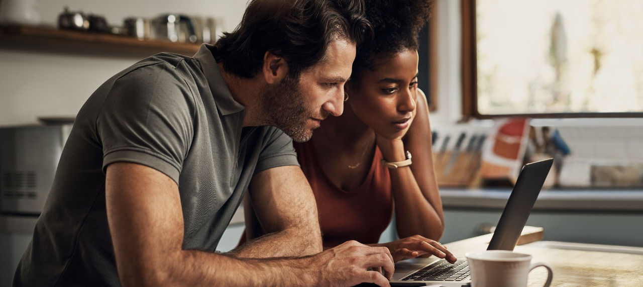 A couple look at their laptop in their kitchen.