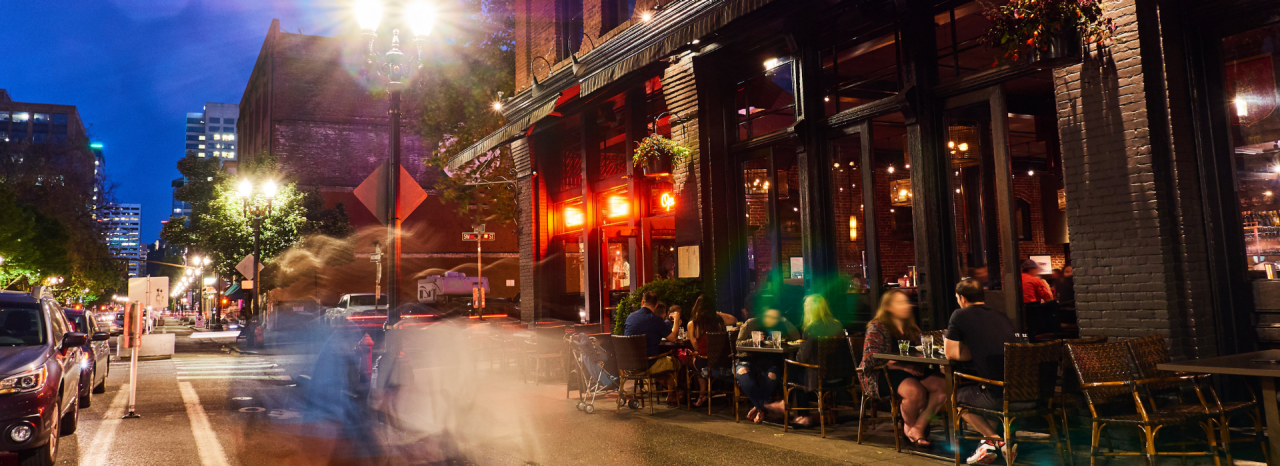 Escena callejera de la ciudad de Nueva York con gente comiendo en un restaurante al aire libre por la noche. 
