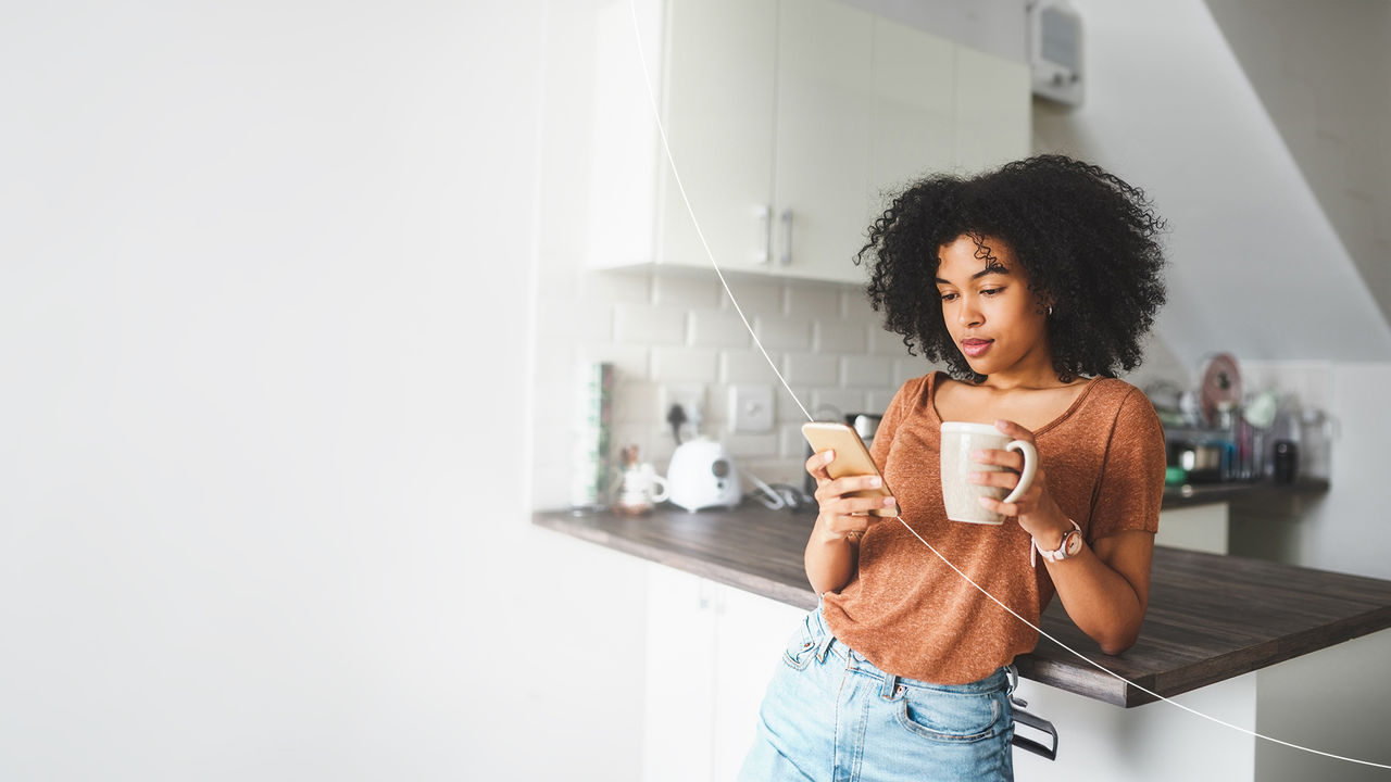 woman with coffee cup using phone in the kitchen.