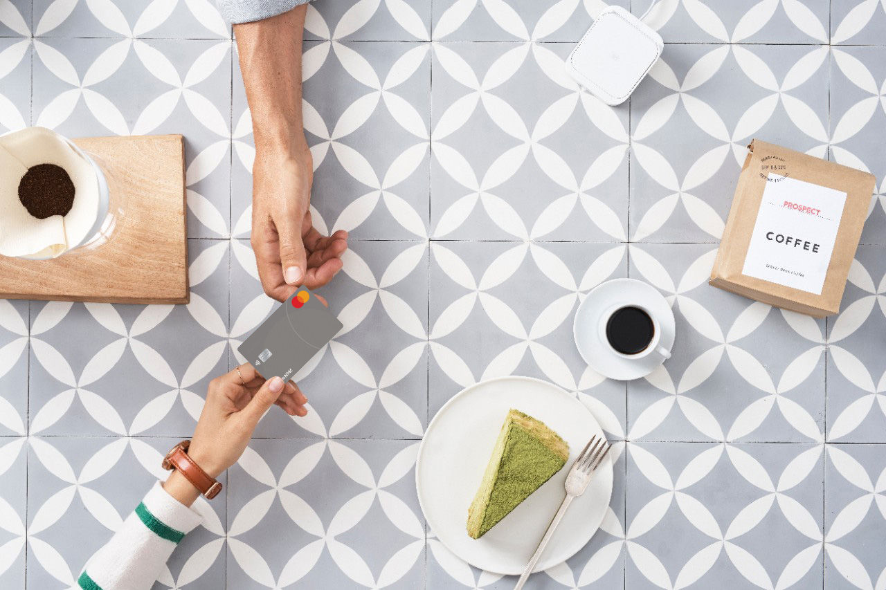 Kupac koji drži Mastercard, spreman da plati na POS terminalu za stolom u kafiću.