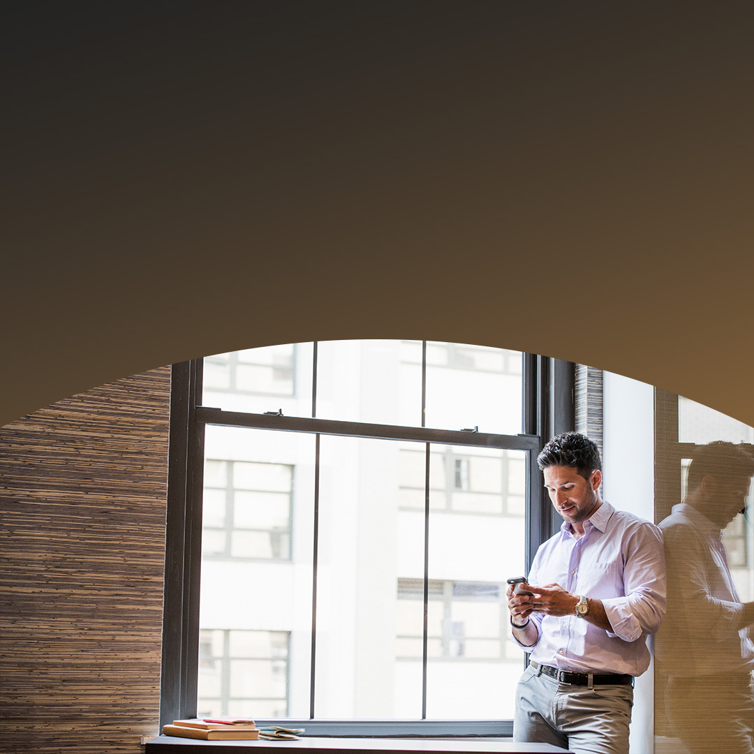 Čovek koristi telefon da bi pronašao najnovije vesti pored prozora u kancelariji.