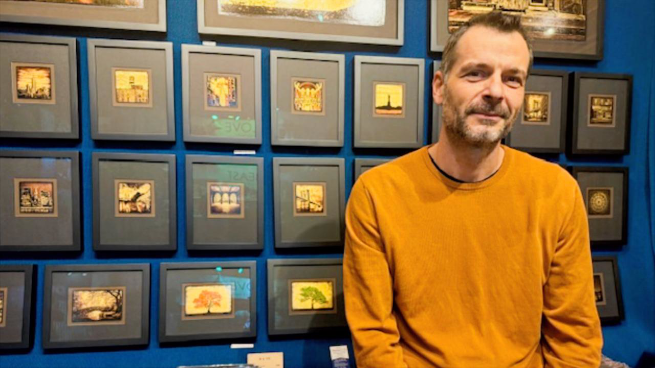 Djordje Skendzic, Skendzic Photography, stands in front of framed prints at Grand Central's market. 