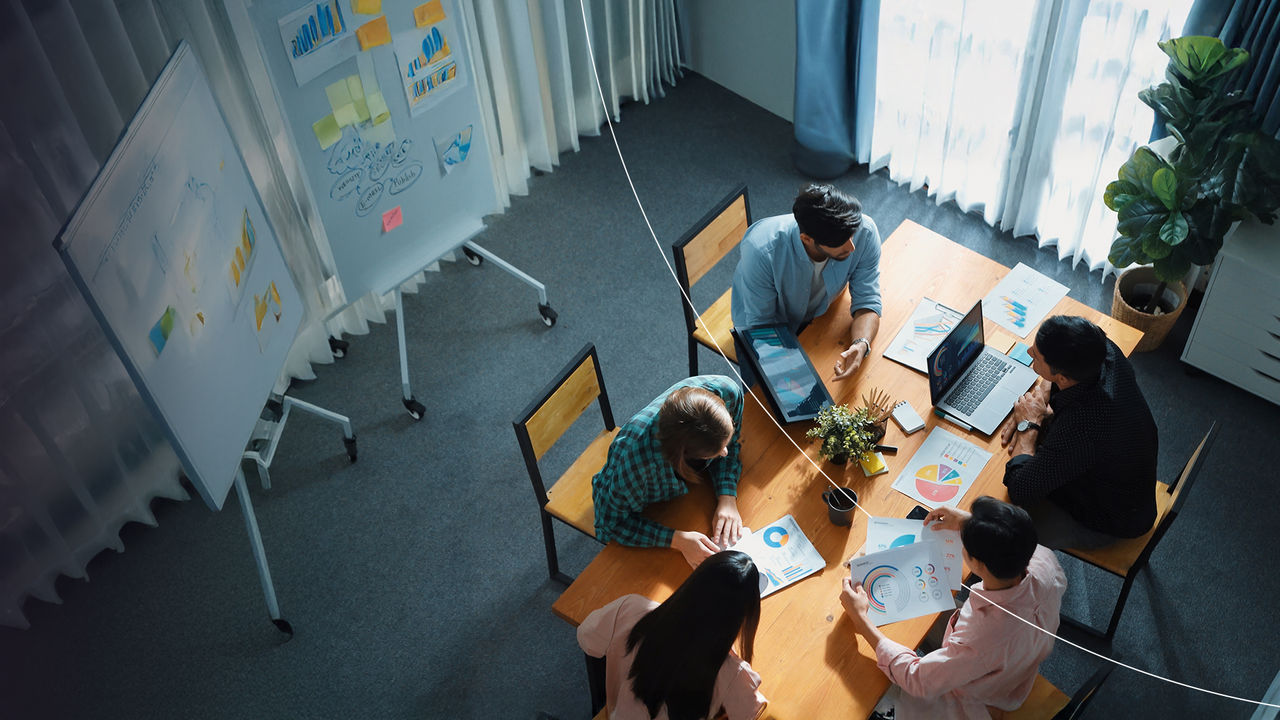 Overhead view of coworkers in a meeting room discussing documents and charts at a table.