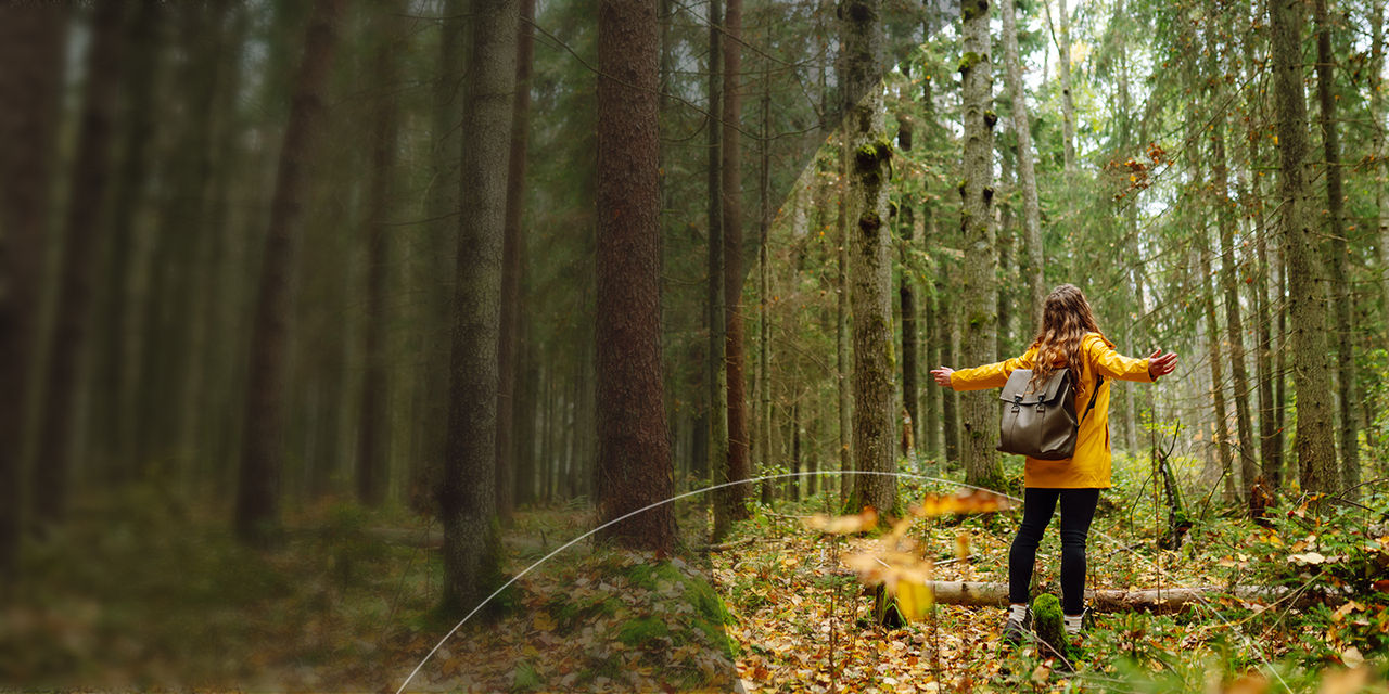 Kvinna i gul jacka som står i en tät skog.