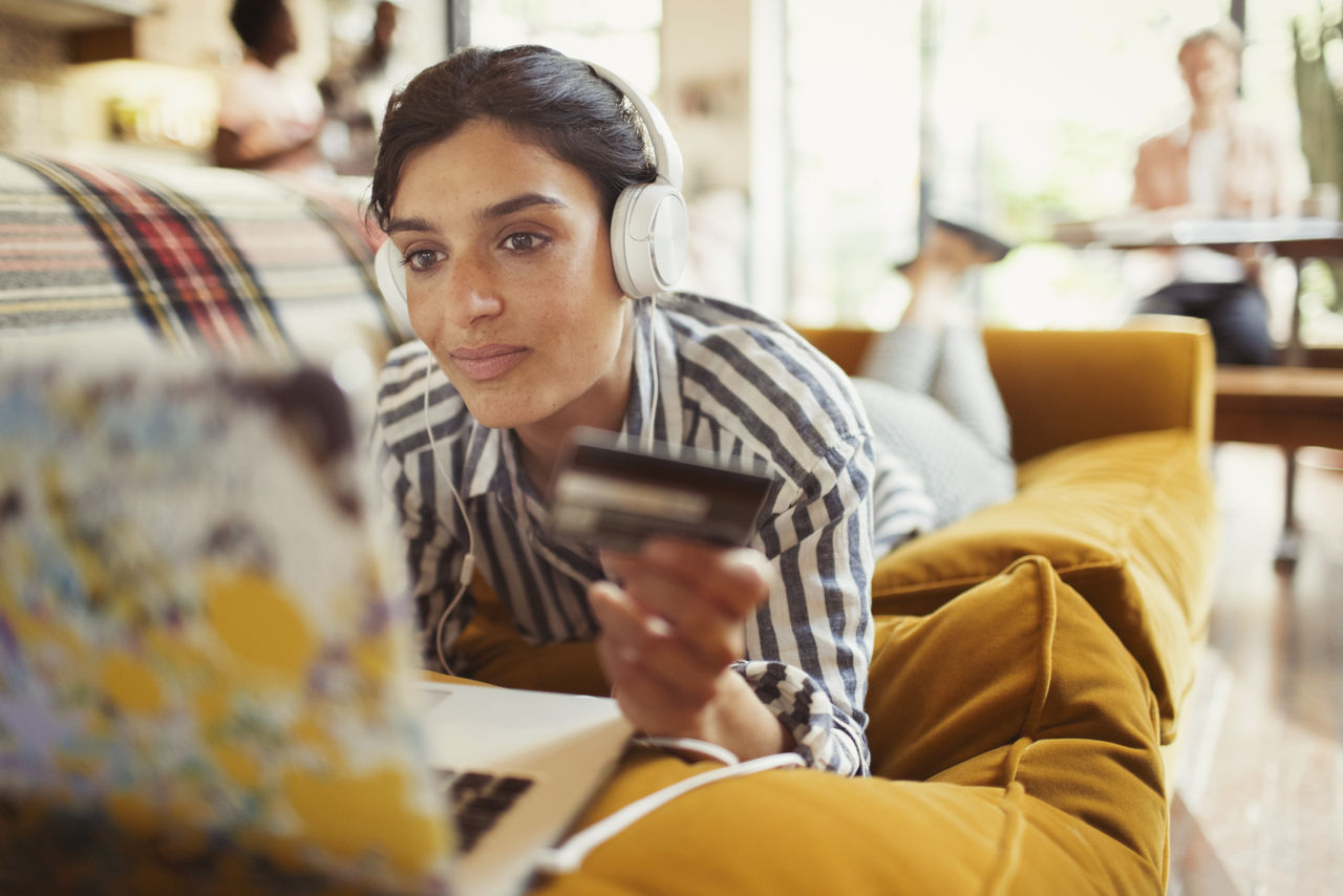 Young woman credit card headphones online shopping at laptop on sitting room sofa