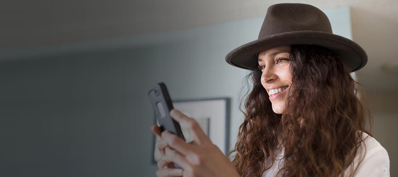Woman with hat holding her phone and smiling