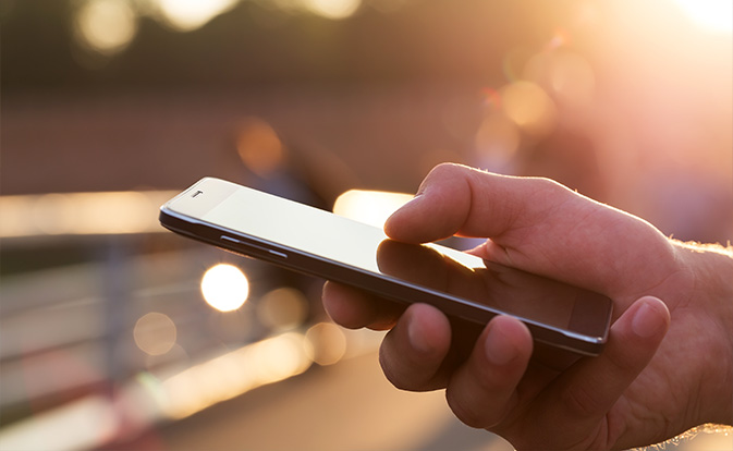 A person holding a mobile phone in their hand, looking at the screen with a focused expression.