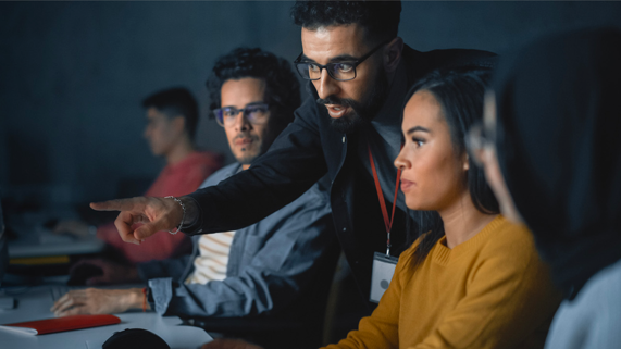 A teacher instructs three focused students in a dimly lit classroom.