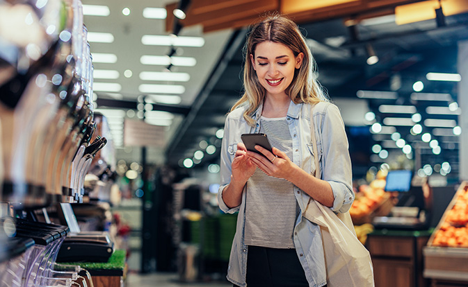 Woman smiling while using her smartphone in a public space.