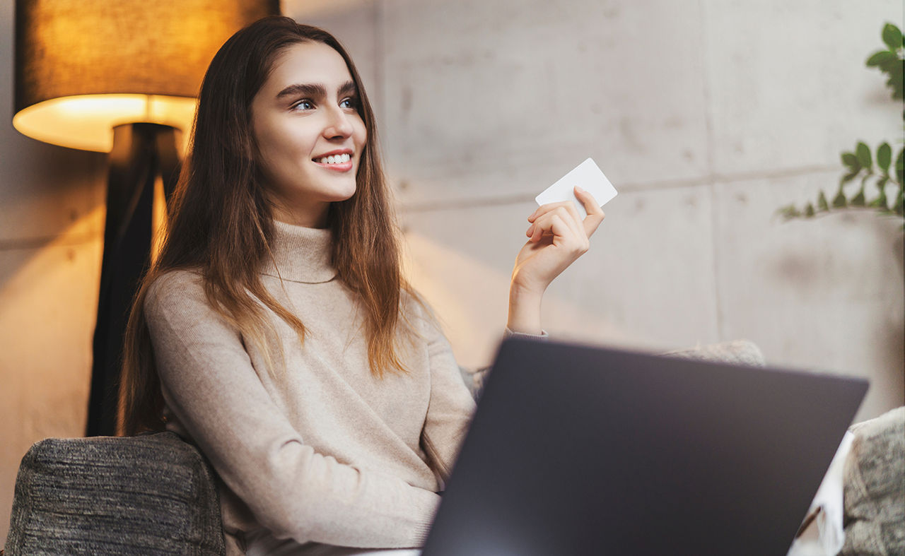 Woman holds payment card while sitting in front of laptop