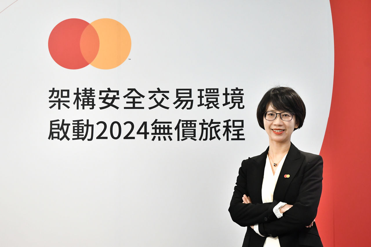 A woman in a black blazer stands with her arms crossed, smiling in front of a white and red backdrop with Chinese text and a brand logo.