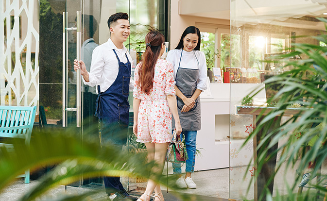 Cheerful vietnamese waiters welcoming cafe guest