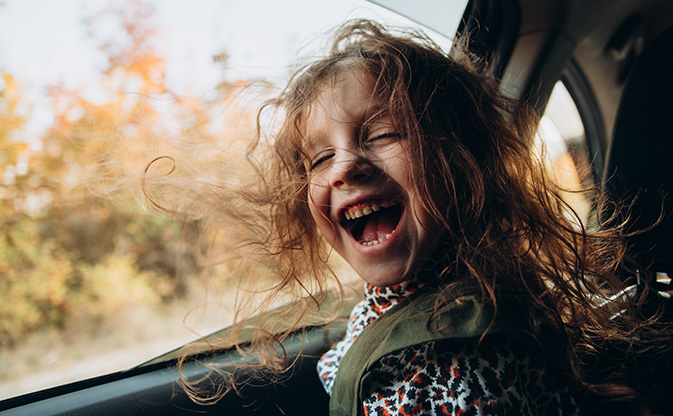 Child sitting in a car with open windows and hair blowing in the wind.