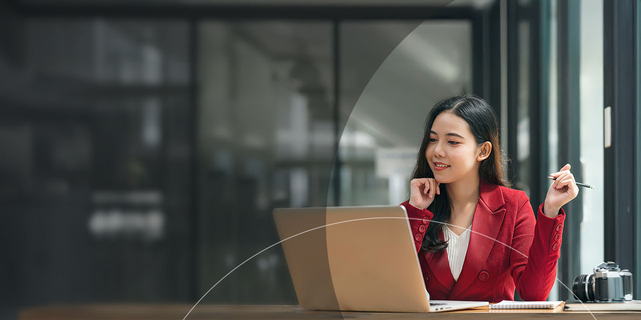 Woman holding pen while looking at laptop in office.