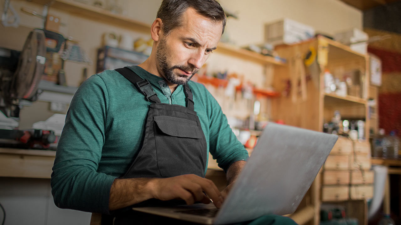 A mature worker using a laptop in carpenter's workshop.