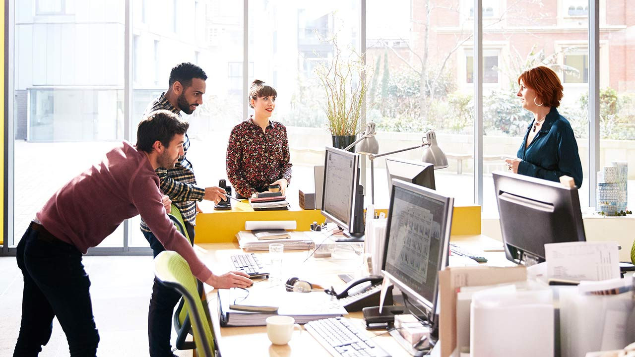 Coworkers talking over ideas in open plan office.