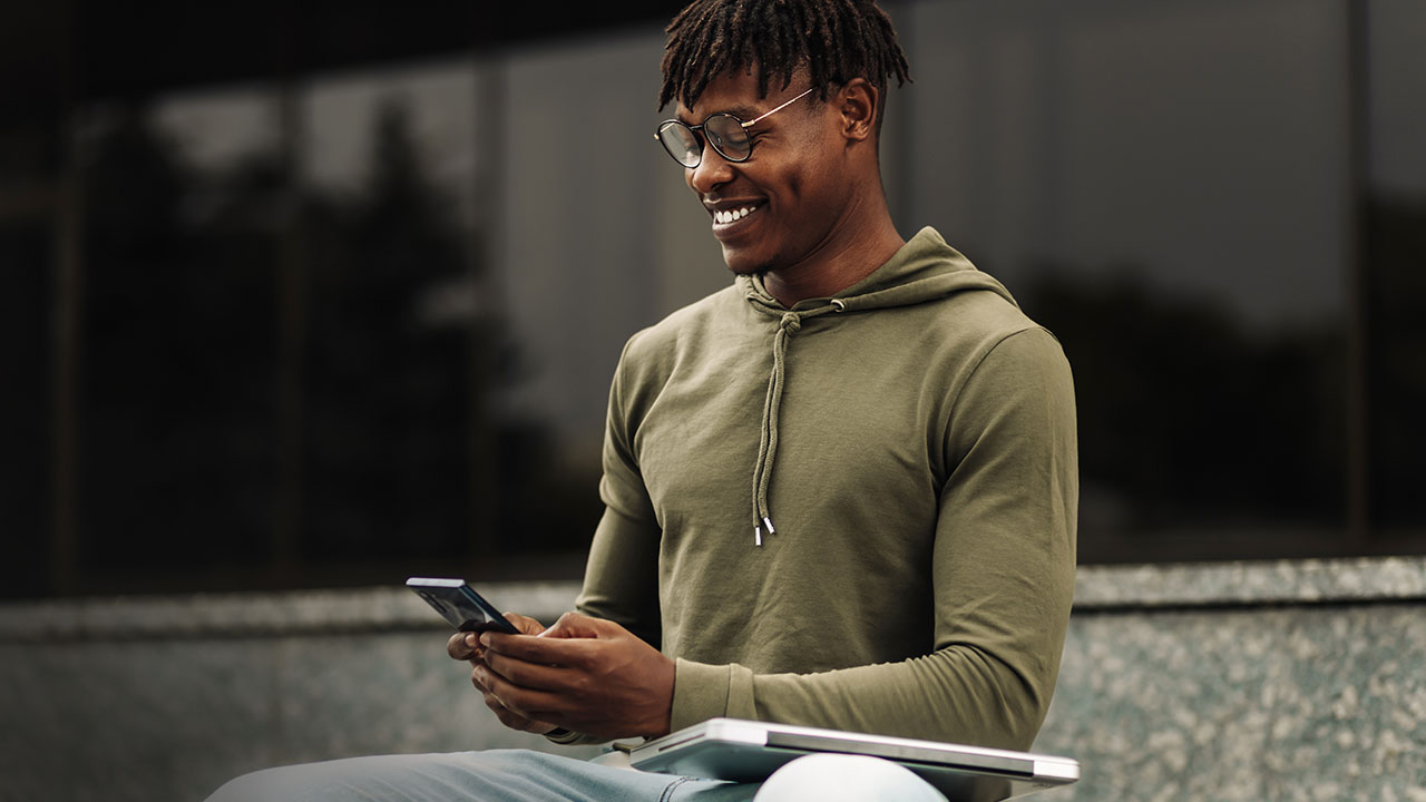 Man using mobile phone, holding laptop outdoors.