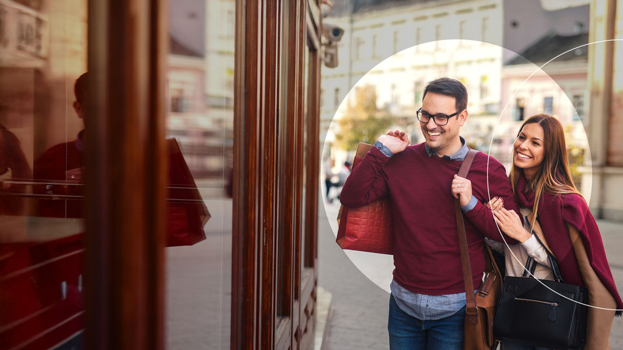 Woman and man carrying shopping bags while walking down the street.