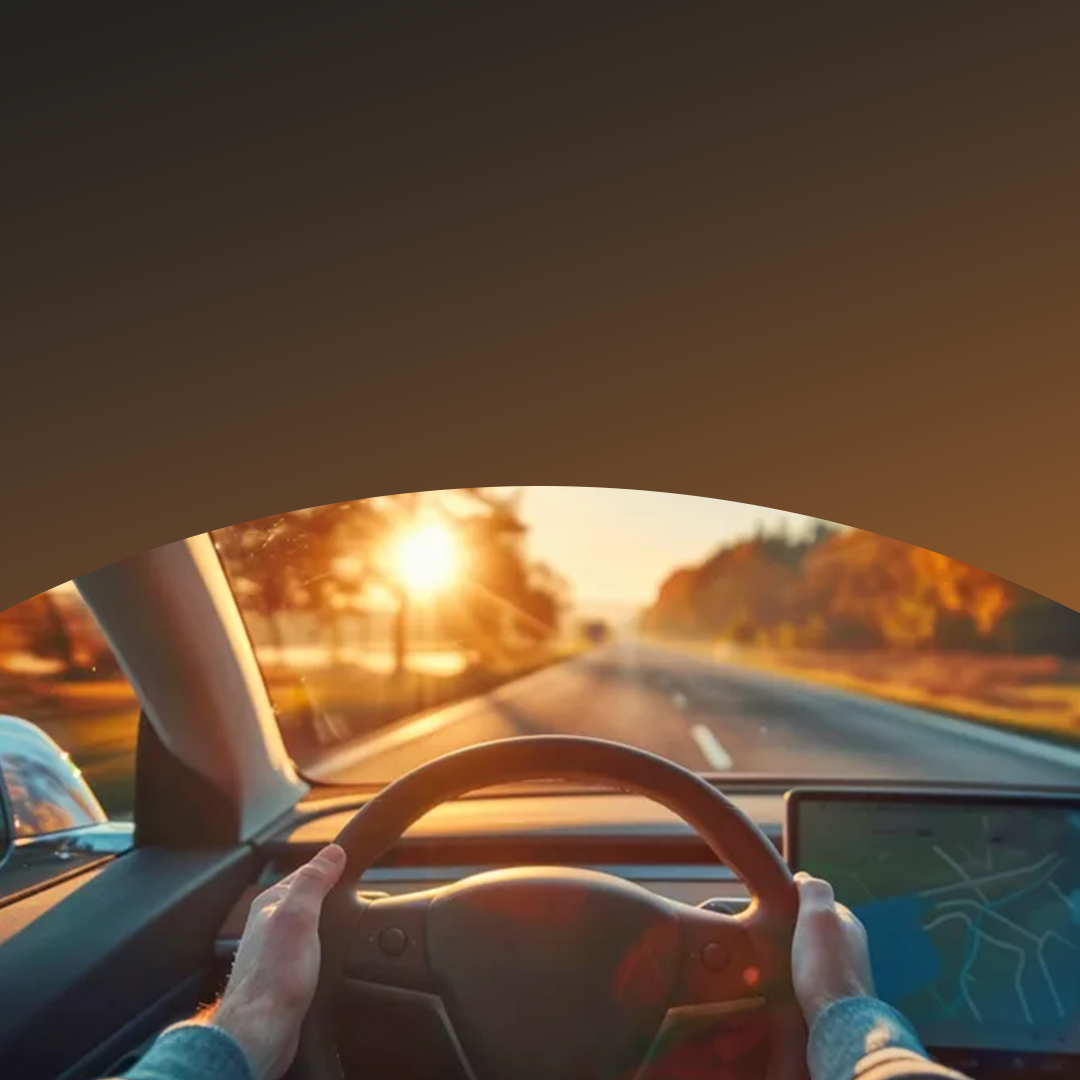Hands on steering wheel driving at sunset.