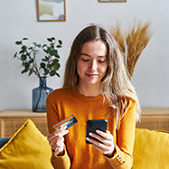 Woman sitting on couch using her card on her phone.