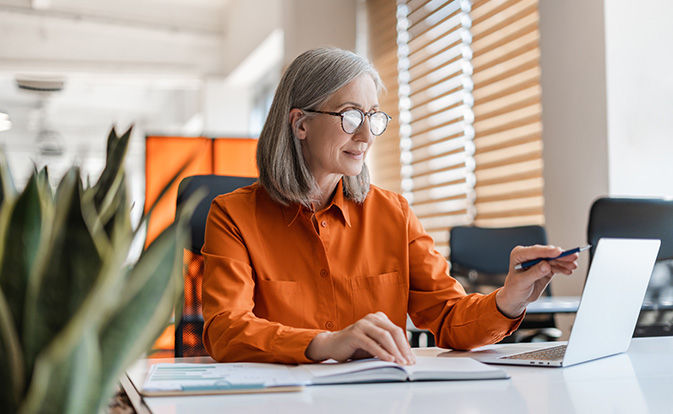 Woman at her desk, focused on reviewing details on her laptop.