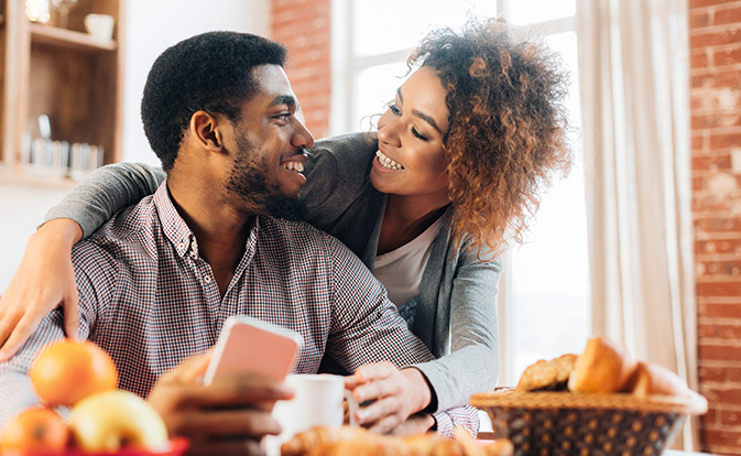 Couple sharing a warm moment, smiling at each other while holding coffee and a phone.
