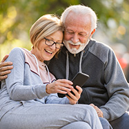 Happy senior couple relaxing in park looking at phone.