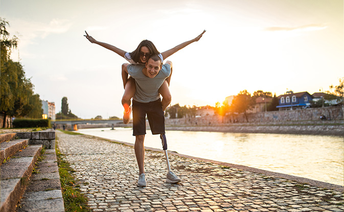 A man with a prosthetic leg carrying a cheering woman on his back.