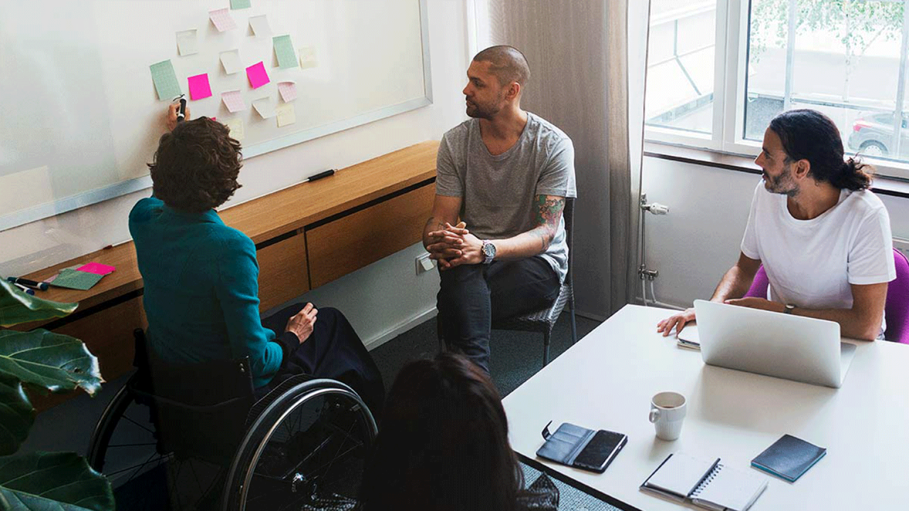 Three people working at a white board with post it notes.