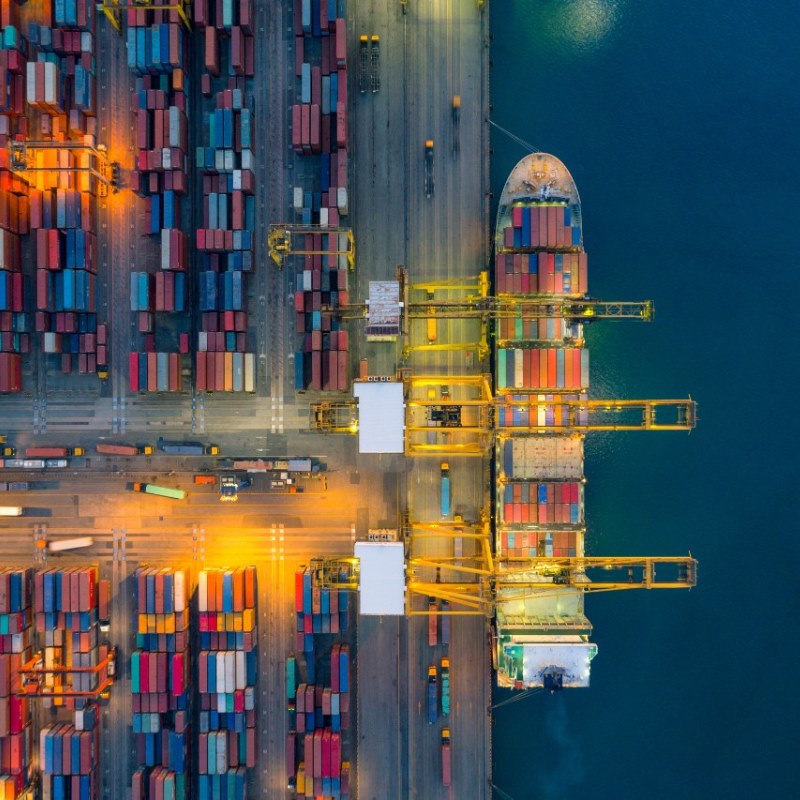 An overhead shot of a cargo ship being loaded at at dock. 