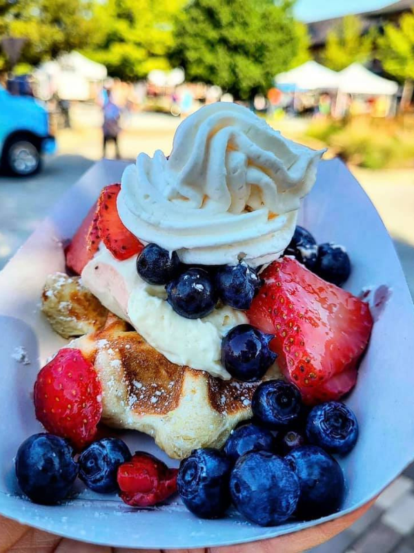 A waffle covered with strawberries, blueberries and whipped cream on a plate. 