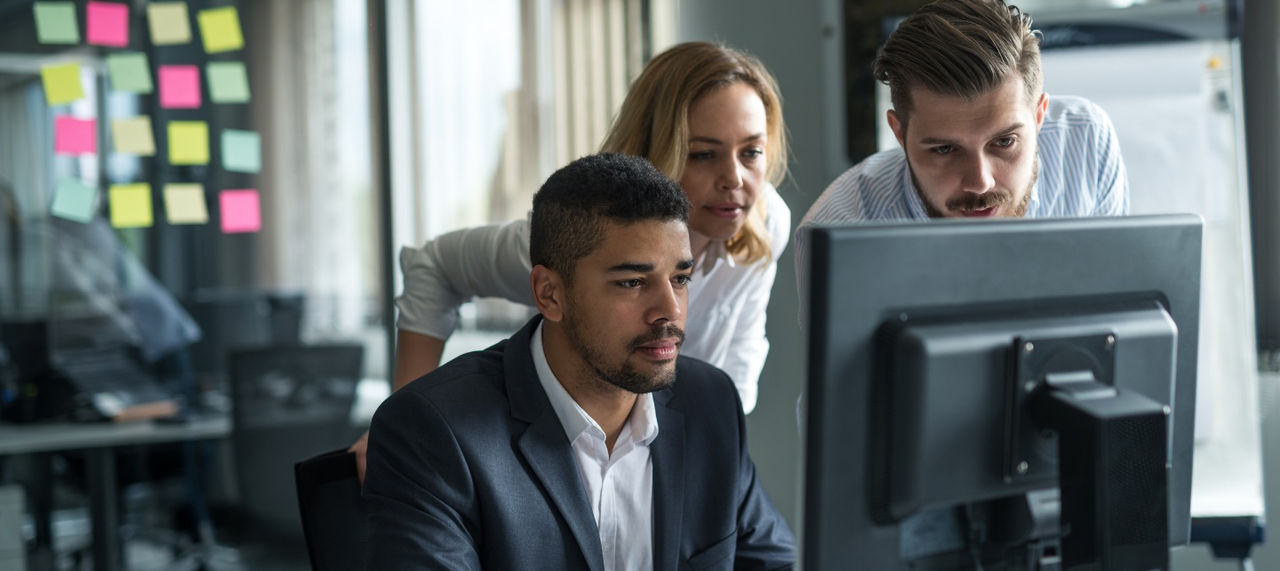 Three employees look at a computer with concern. 