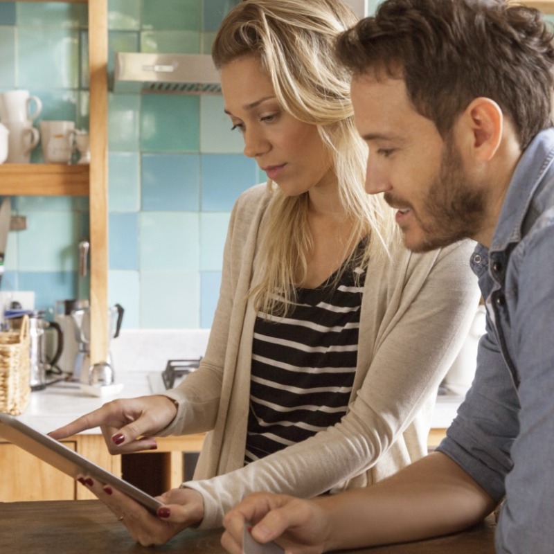 A man and a woman look at a tablet in a kitchen. 