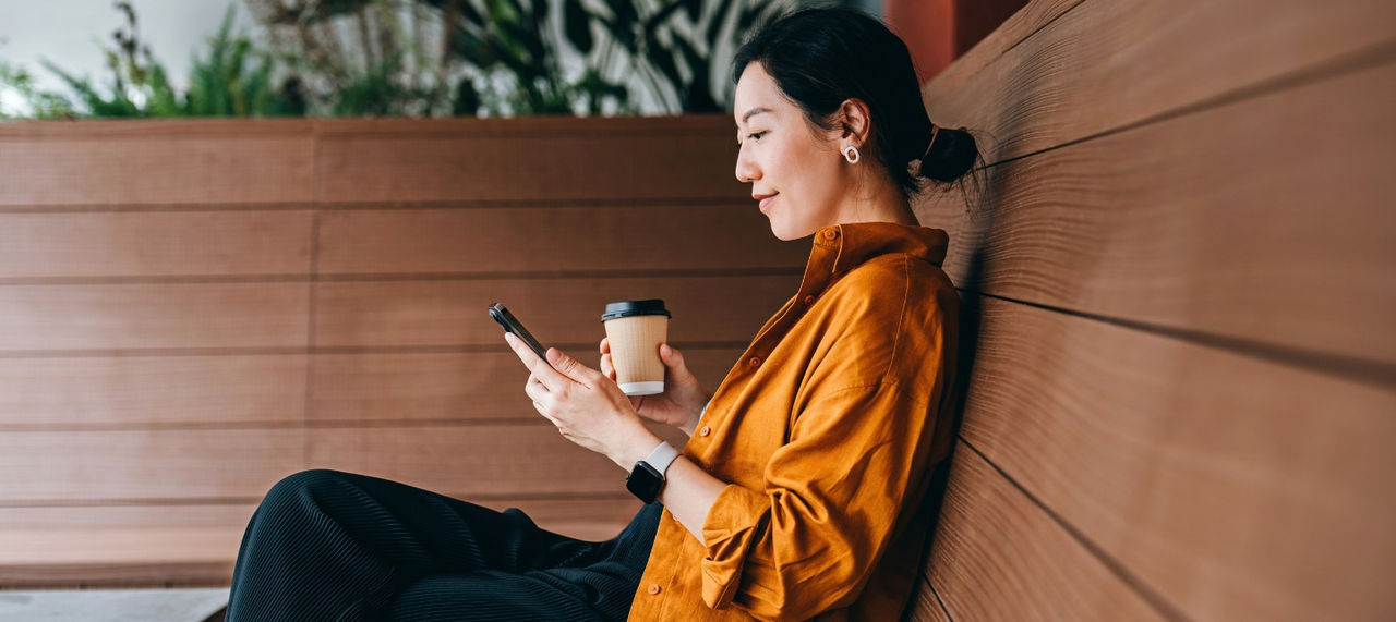 A woman sits on a bench and smiles at her phone. 