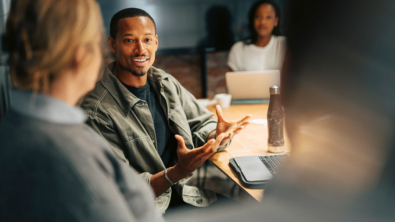 smiling man gesturing while talking to colleagues in a meeting