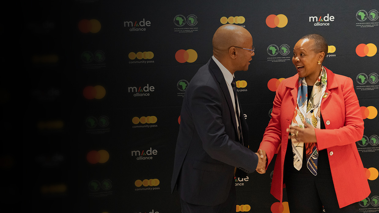 A man and woman shaking hands in front of a board of logos.